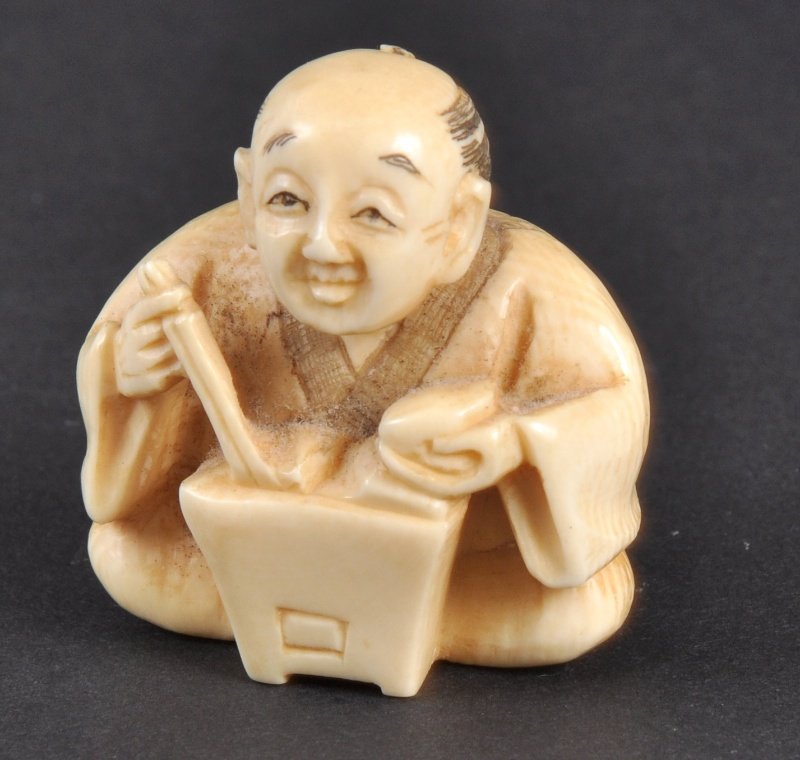 A CARVED IVORY NETSUKE OF A MAN EATING. : A CARVED IVORY NETSUKE OF A MAN EATING.