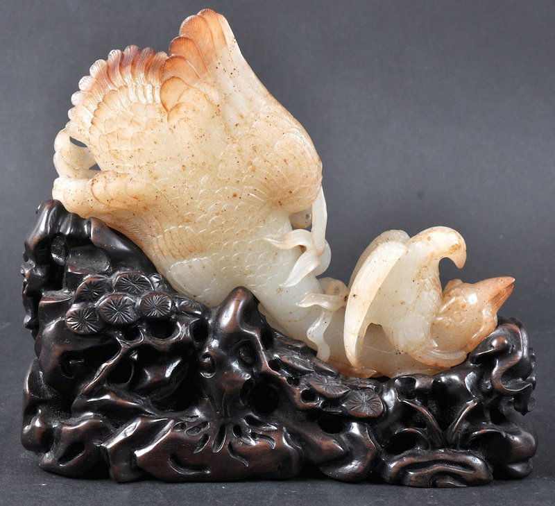 AN EARLY 20TH CENTURY CHINESE WHITE RUSSET JADE C: AN EARLY 20TH CENTURY CHINESE WHITE RUSSET JADE CARVED BIRD modelled with another perched upon its back, supported on a fitted hardwood stand. Natural fissures. Jade 5.5ins wide.