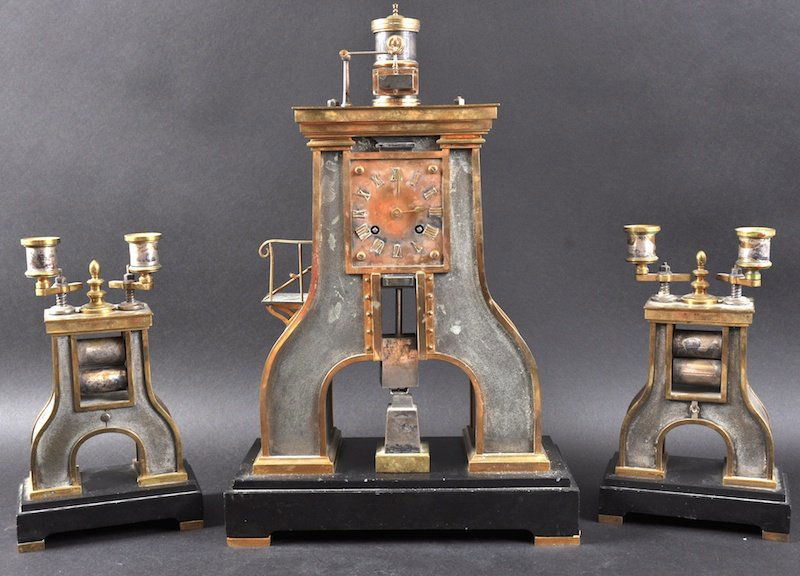 A FINE 19TH CENTURY FRENCH INDUSTRIAL ‘STEAM HAMMER’ C: A FINE 19TH CENTURY FRENCH INDUSTRIAL ‘STEAM HAMMER’ CLOCK GARNITURE BY GUILMET with eight day time and bell strike, the dial with applied Roman numerals. Clock 1ft 5. 5ins high. (3)