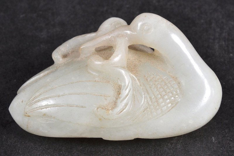 A CHINESE QING DYNASTY CARVED WHITE JADE FIGURE OF A CR: A CHINESE QING DYNASTY CARVED WHITE JADE FIGURE OF A CRANE modelled with a lotus leaf upon its mouth. Small nick to leaf. 2ins wide.