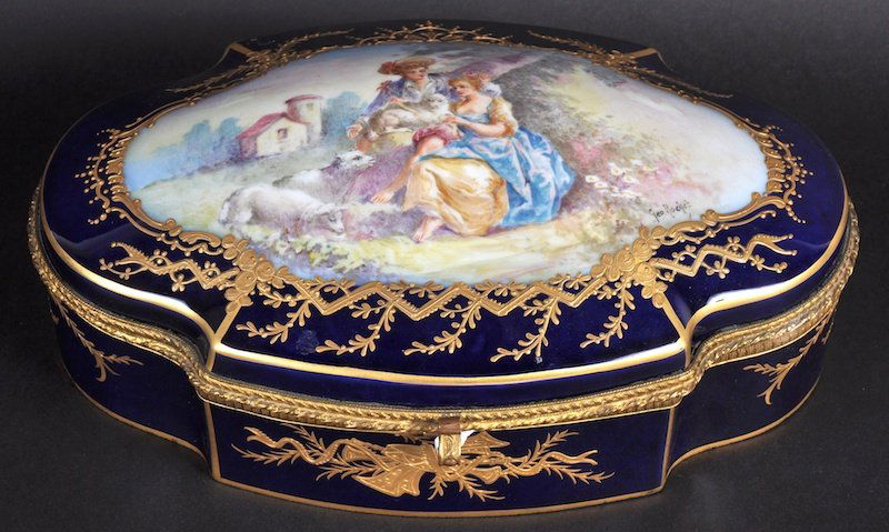 A GOOD SEVRES BLUE OVAL SHAPED CASKET with gilt decora: A GOOD SEVRES BLUE OVAL SHAPED CASKET with gilt decoration, the top painted with a shepherd girl and boy with lambs by GEORGE ROCHET, Chateau des Tuileries stamp to base.9.5ins long.