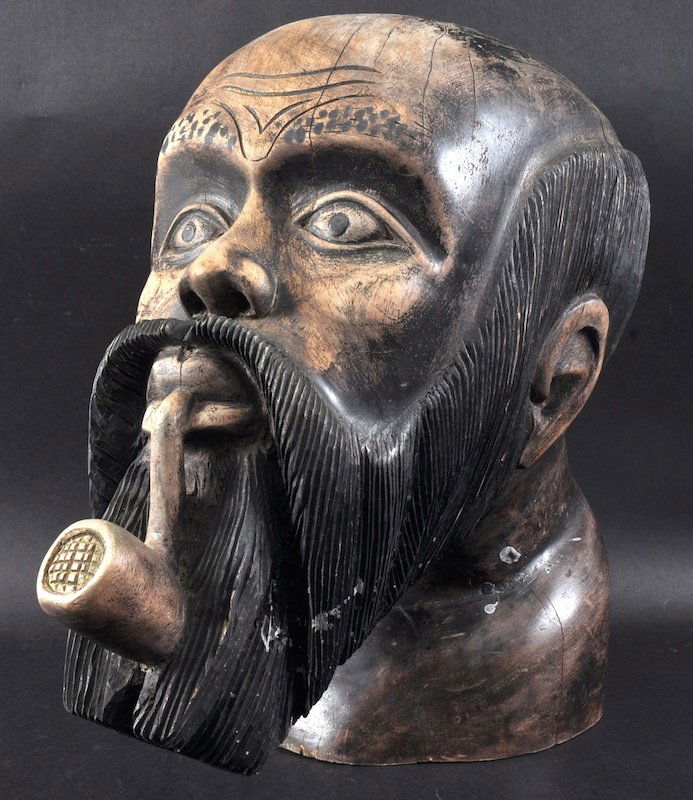 A MALAYAN CARVED WOOD TOBACCO SHOP SIGN as a MAN WITH A: A MALAYAN CARVED WOOD TOBACCO SHOP SIGN as a MAN WITH A PIPE IN HIS MOUTH. 18ins high. Bears white label ALFRED DUNHILL OF LONDON.