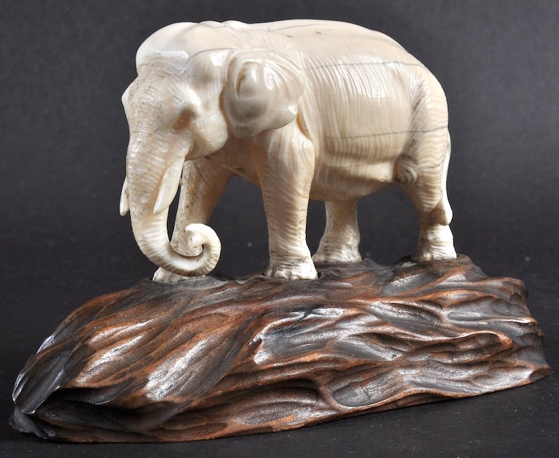 A LATE 19TH CENTURY JAPANESE MEIJI PERIOD IVORY OKIMONO: A LATE 19TH CENTURY JAPANESE MEIJI PERIOD IVORY OKIMONO depicting an elephant roaming, upon a fitted hardwood base. Natural flaws. Ivory 4ins wide.