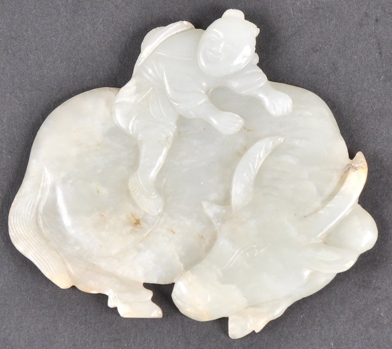 A CHINESE QING DYNASTY HETIAN JADE PLAQUE carved as a: A CHINESE QING DYNASTY HETIAN JADE PLAQUE carved as a young boy climbing aloft a finely formed recumbent buffalo. Nick to horn. 2.75ins x 2.25ins.