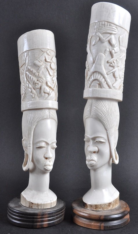 A PAIR OF WHITE IVORY AFRICAN TUSK VASES as female: A PAIR OF WHITE IVORY AFRICAN TUSK VASES as female heads carrying baskets. 15 x 13ins high.