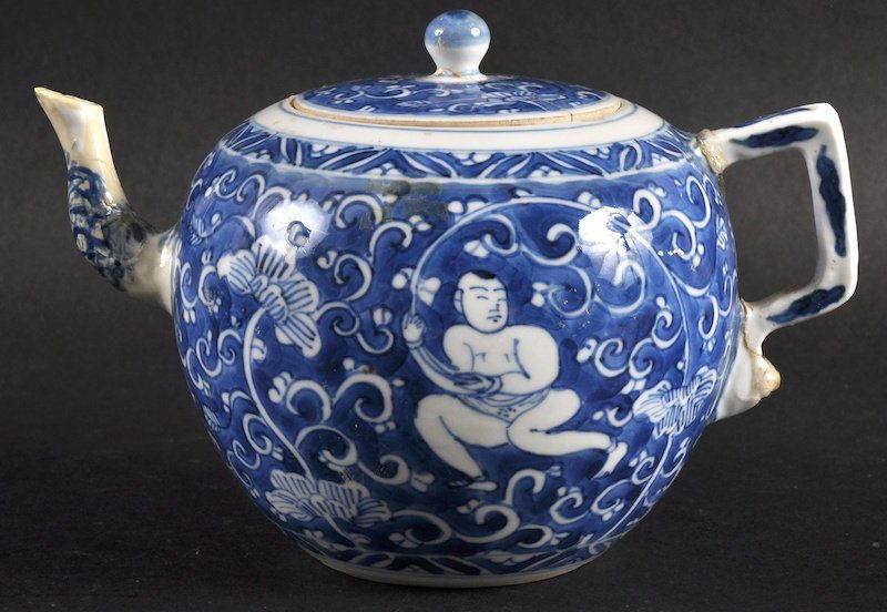 A LATE 17TH CENTURY CHINESE BLUE AND WHITE TEAPOT AND: A LATE 17TH CENTURY CHINESE BLUE AND WHITE TEAPOT AND COVER Kangxi, painted with figures amongst bands of foliage. Repaired. 6ins wide.