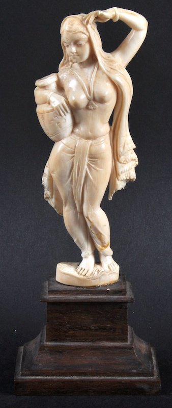 AN INDIAN CARVED IVORY FIGURE OF A YOUNG LADY carrying: AN INDIAN CARVED IVORY FIGURE OF A YOUNG LADY carrying a pitcher. 5.25ins high, on a wooden plinth.
