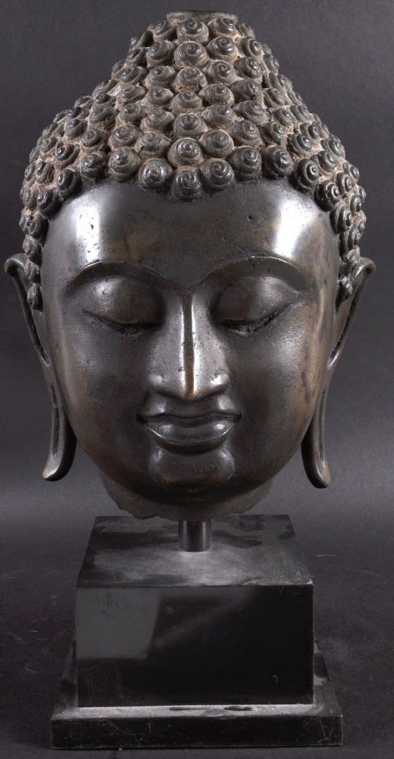 AN 18TH CENTURY SOUTH EAST ASIAN BRONZE BUST OF BUDDHA: AN 18TH CENTURY SOUTH EAST ASIAN BRONZE BUST OF BUDDHA modelled with a sureen expression, supported upon a stepped base. Bronze 1ft 2ins high.