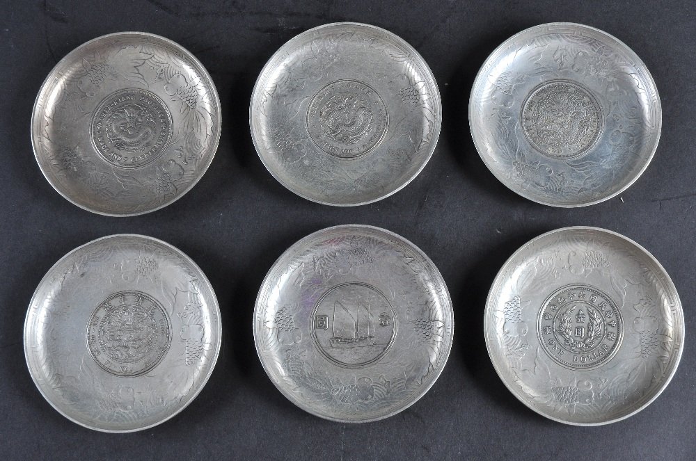 A SET OF CHINESE WHITE METAL CIRCULAR DISHES inset with: A SET OF CHINESE WHITE METAL CIRCULAR DISHES inset with coins, possibly Republican period. 3.75ins diameter. (6)