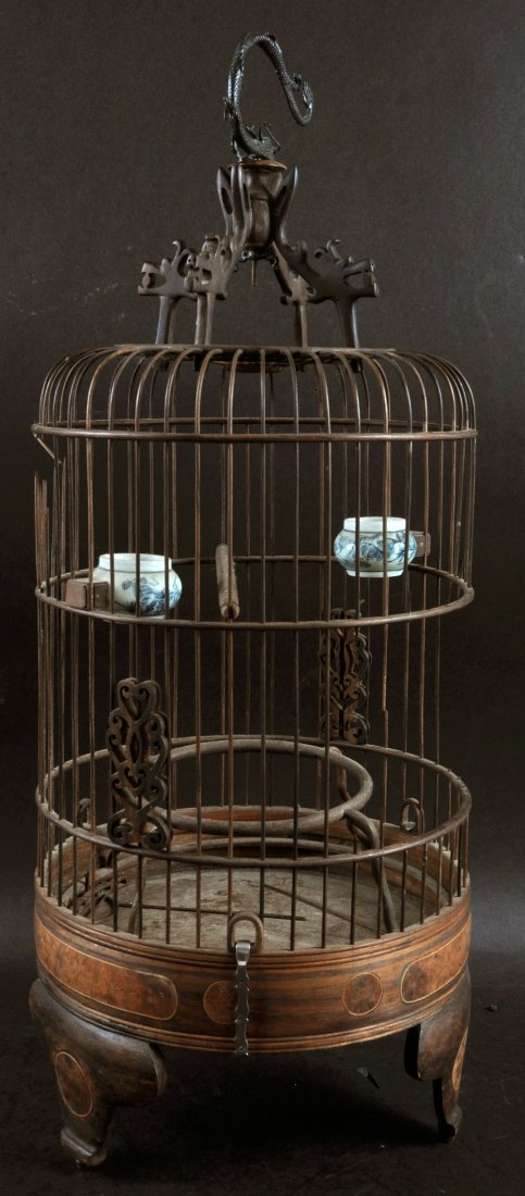 A CHINESE WOOD BIRD CAGE, with a metal dragon form: A CHINESE WOOD BIRD CAGE, with a metal dragon form hanging hook, the interior with two porcelain feeding bowls, 21.5in high.