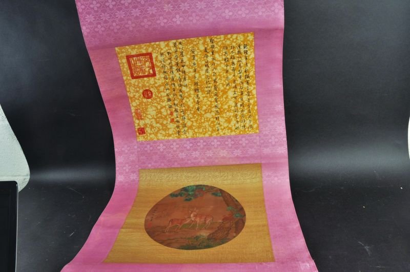 A CHINESE SCROLL PAINTING ON SILK, mounted on a: A CHINESE SCROLL PAINTING ON SILK, mounted on a patterned silk ground, the circular painting depicting deer standing beneath overhanging pine, the scroll 26.25in wide including wood endpieces.