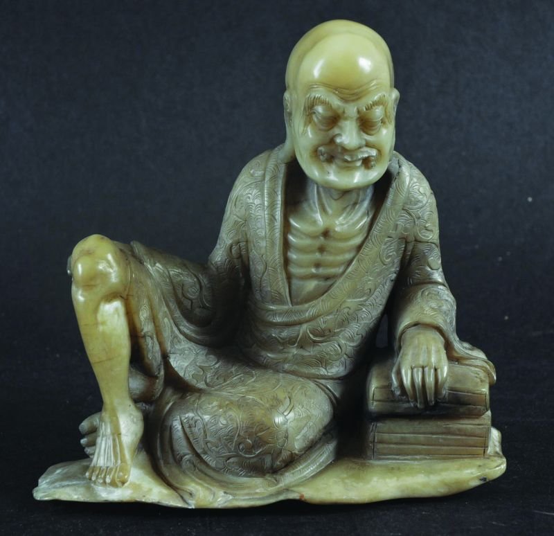 A CHINESE CARVED SOAPSTONE FIGURE OF A RECLINING LOHAN,: A CHINESE CARVED SOAPSTONE FIGURE OF A RECLINING LOHAN, his robes with detailed engraving, 4.1in wide & 4in high.