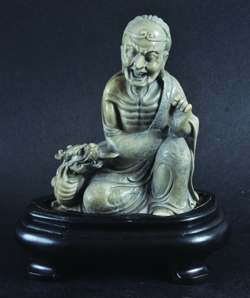 A CHINESE CARVED SOAPSTONE FIGURE OF A SEATED SAGE IN: A CHINESE CARVED SOAPSTONE FIGURE OF A SEATED SAGE IN THE COMPANY OF A DRAGON, the sage’s robes with detailed engraving, together with a fitted wood stand, the soapstone 3.75in wide & 4.6in high. (2