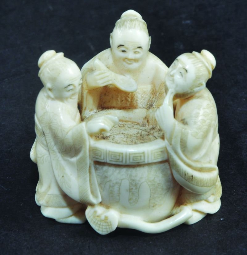 A LATE 19TH CENTURY SIGNED JAPANESE NETSUKE, of three: A LATE 19TH CENTURY SIGNED JAPANESE NETSUKE, of three men sipping form a cauldron, the base with an inlaid red lacquer signature plaque, 1.5in high