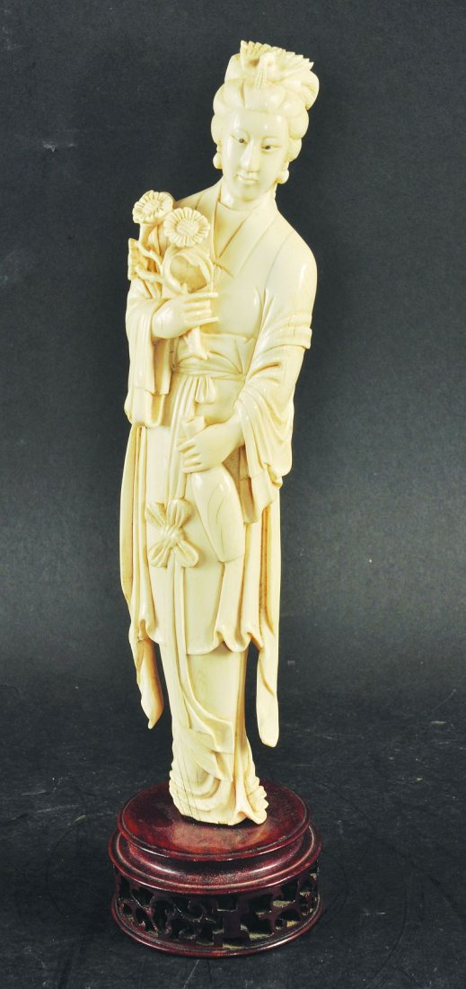 AN EARLY 20TH CENTURY CHINESE IVORY CARVING OF A LADY,: AN EARLY 20TH CENTURY CHINESE IVORY CARVING OF A LADY, mounted on a hardwood stand, the lady holding a vase in one hand and a floral spray in the other, the ivory 10in high. £250-350