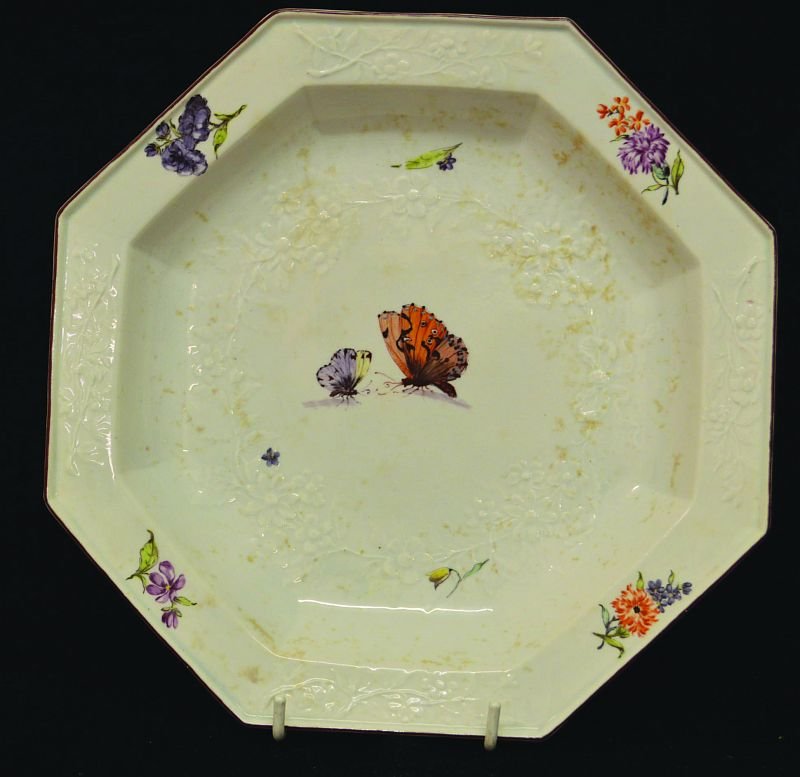 A CHELSEA GOTZKOWSKY MOULDED WHITE GROUND OCTAGONAL: A CHELSEA GOTZKOWSKY MOULDED WHITE GROUND OCTAGONAL PLATE, CIRCA. 1754, painted with flowers and butterflies. 9.25ins diameter. £100-150.