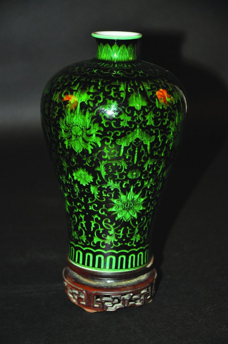 A CHINESE GREEN GLAZED BLACK-GROUND MEIPING PORCELAIN: A CHINESE GREEN GLAZED BLACK-GROUND MEIPING PORCELAIN VASE, together with a carved wood stand, the vase decorated with an overall formal design of scroll and leaf-stemmed foliage, the base with a six-