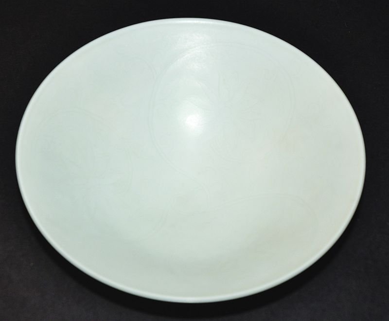 A CHINESE WHITE GLAZED PORCELAIN BOWL, of early form: A CHINESE WHITE GLAZED PORCELAIN BOWL, of early form and design, the interior with underglaze incised decoration of formal scroll-stemmed foliage, the base with a four-character mark, 6.25in diameter.