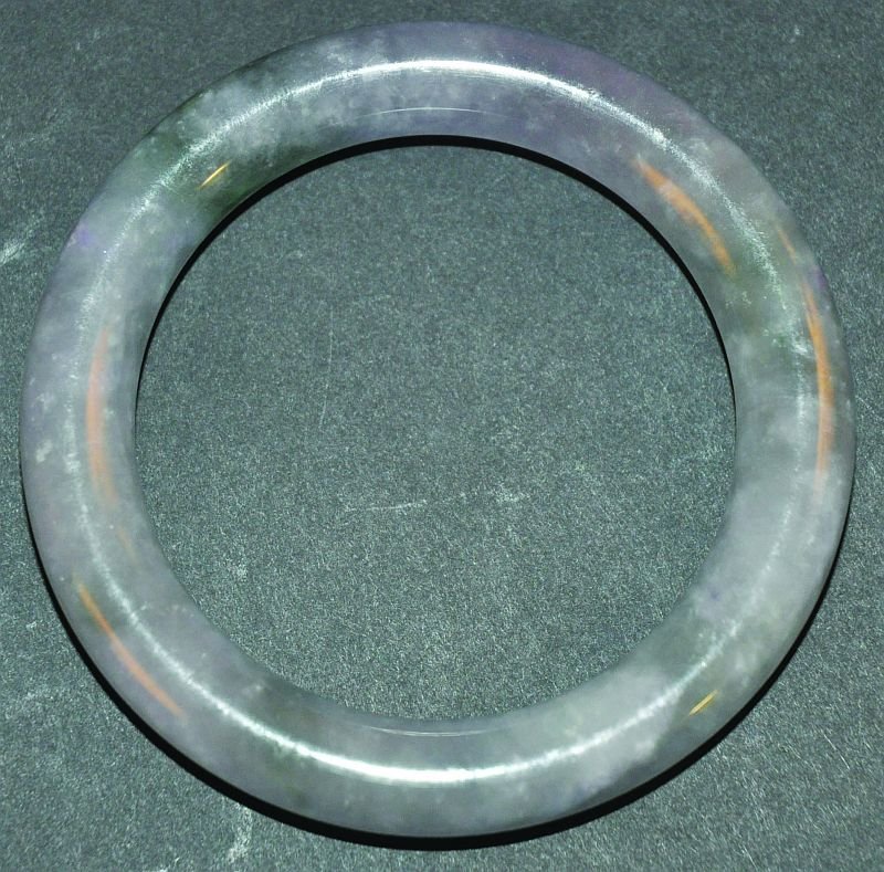 A CHINESE JADE BANGLE, the predominantly mottled green: A CHINESE JADE BANGLE, the predominantly mottled green stone with white and purple inclusions, 3.1in diameter, inner rim 2.25in diameter. £30-50