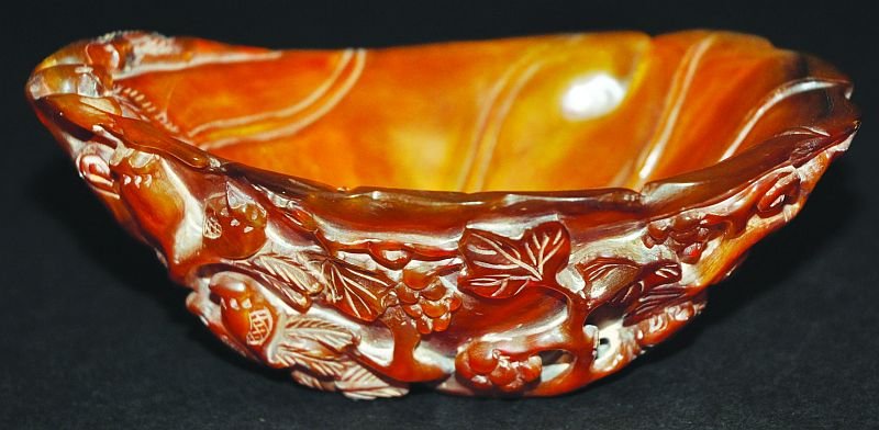 A 20TH CENTURY CHINESE CARVED HORN LIBATION BOWL, the: A 20TH CENTURY CHINESE CARVED HORN LIBATION BOWL, the sides carved in relief with squirrels, pomegranate and vines, 5.6in long & 2.3in high. £100-150