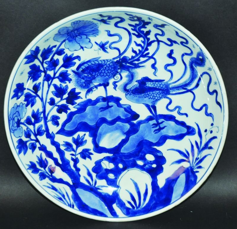 A CHINESE KANGXI PERIOD BLUE & WHITE PORCELAIN CHARGER,: A CHINESE KANGXI PERIOD BLUE & WHITE PORCELAIN CHARGER, circa 1700, the saucer shaped body painted in a vivid tone of underglaze-blue with a pair of phoenix standing on rockwork, 13.3in diameter. £10
