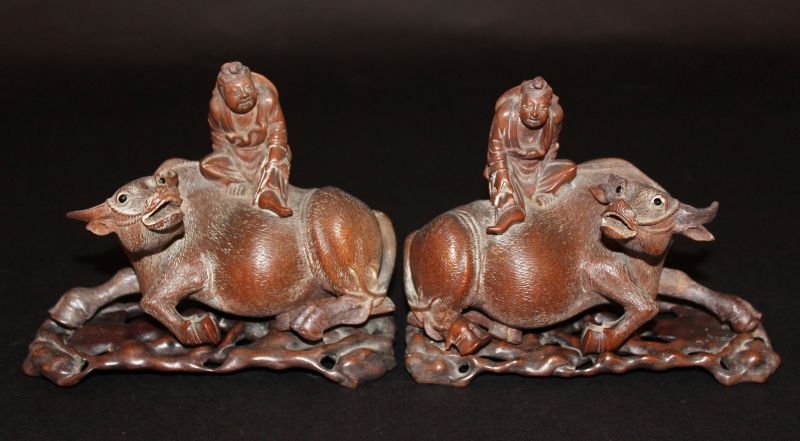 A PAIR OF 19TH CENTURY CHINESE CARVED HARDWOOD: A PAIR OF 19TH CENTURY CHINESE CARVED HARDWOOD BUFFALOS, each carved with a boy seated upon its back, together with a pair of pierced wood stands, the stands 6in long, the buffalos 5.75in long. £200-