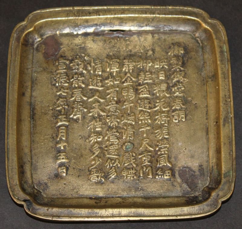 AN EARLY 20TH CENTURY CHINESE BRONZE DISH, supported on: AN EARLY 20TH CENTURY CHINESE BRONZE DISH, supported on four shallow ruyi form feet, the interior with columns of calligraphy, the base with a character mark encircled by two dragons, 5.3in square. £