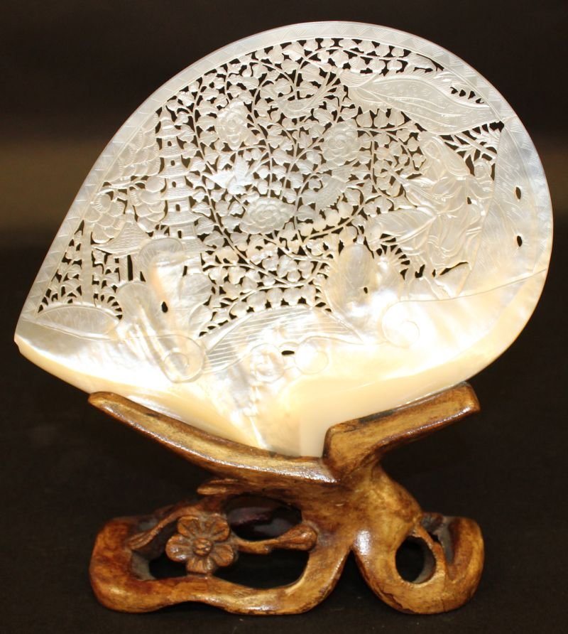 AN EARLY 20TH CENTURY CHINESE CARVED & PIERCED: AN EARLY 20TH CENTURY CHINESE CARVED & PIERCED MOTHER-OF-PEARL SHELL, together with a fitted wood stand, the shell decorated with buildings and a horse rider reserved on a ground of leaf-stemmed folia