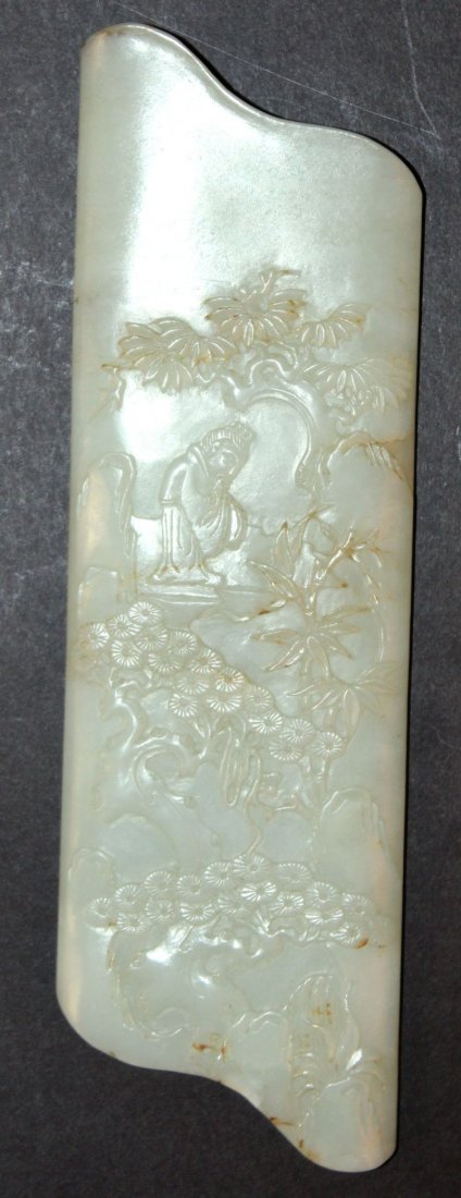 A CHINESE CARVED AND SHAPED-END CELADON-GREEN JADE: A CHINESE CARVED AND SHAPED-END CELADON-GREEN JADE PLAQUE, carved in low relief with a sage in a grove of pine and rockwork, 7.5in long.