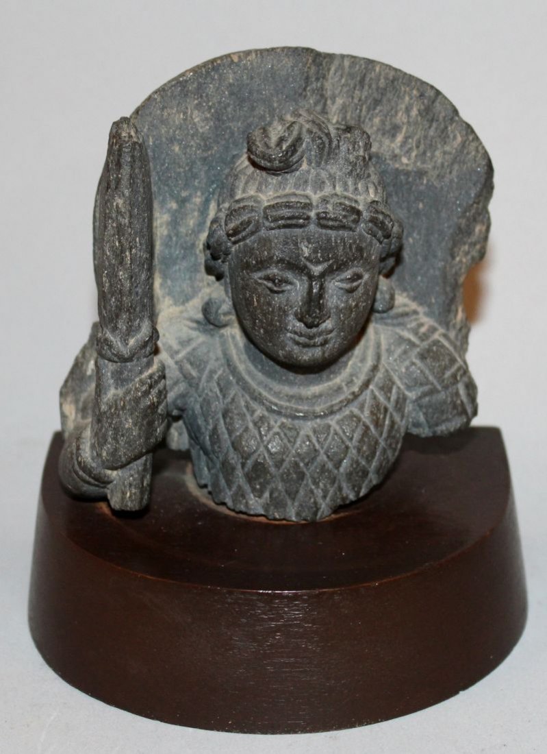 A GANDHARA SCHIST CARVING OF PANCHIKA, mounted on a: A GANDHARA SCHIST CARVING OF PANCHIKA, mounted on a wood base, the deity holding a spear, the base 4.6in wide, the carving itself 3.75in high. £100-150