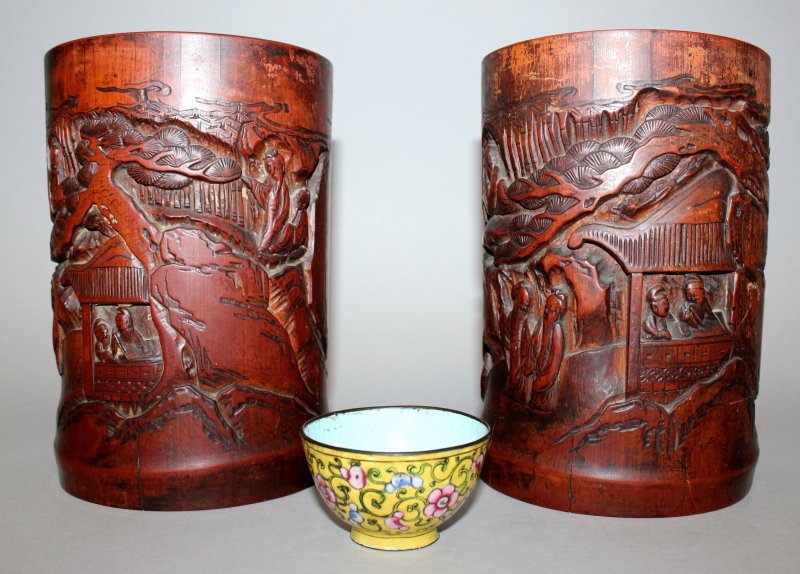 A PAIR OF EARLY 20TH CENTURY CHINESE CARVED BAMBOO: A PAIR OF EARLY 20TH CENTURY CHINESE CARVED BAMBOO BRUSH POTS, each decorated with a scene of sages, pine and rockwork, 7.2in high; together with a yellow-ground Canton enamel teabowl, 2.6in diameter.