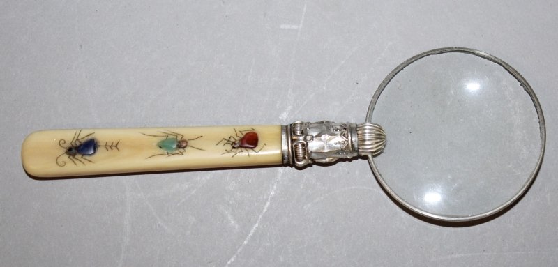 A MAGNIFYING GLASS WITH A JAPANESE SHIBAYAMA IVORY: A MAGNIFYING GLASS WITH A JAPANESE SHIBAYAMA IVORY HANDLE, inlaid with three insects, 5.9in long. John Nicholsons Auctioneers do not ship items containing ivory to the USA or its territories. £40-60.
