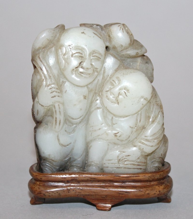 A 19TH CENTURY CHINESE JADE CARVING OF THE HE HE: A 19TH CENTURY CHINESE JADE CARVING OF THE HE HE ERXIAN, together with a fixed wood stand, one of the twin boys standing and holding a lotus frond, the other boy kneeling, 2.3in high, the base 1.9in w