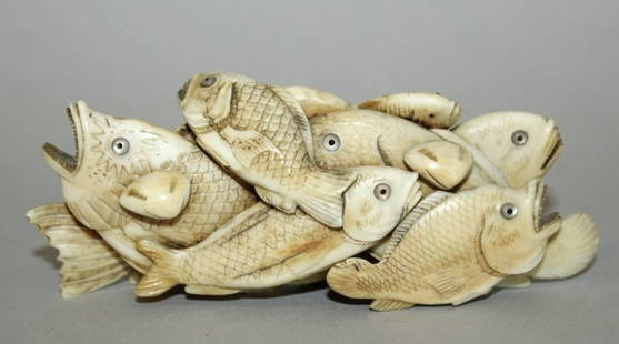 A JAPANESE MEIJI PERIOD CARVED IVORY OKIMONO OF A GROUP: A JAPANESE MEIJI PERIOD CARVED IVORY OKIMONO OF A GROUP OF FISH, unsigned, of various varieties overlapping and intertwined, a crab to one side, their eyes inlaid in mother-of-pearl, 4.75in wide & 2in