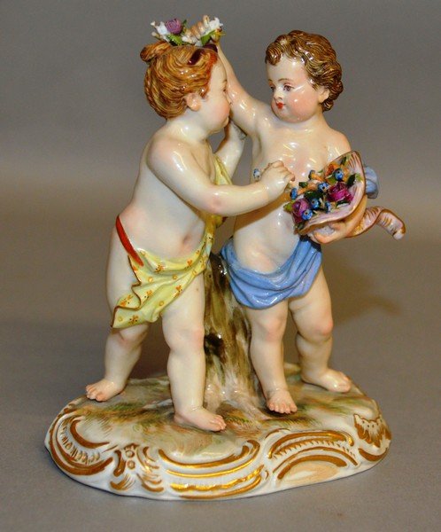 A GOOD SMALL MEISSEN GROUP OF TWO CUPIDS, one with a: A GOOD SMALL MEISSEN GROUP OF TWO CUPIDS, one with a basket of flowers. 4.25ins high. Cross swords mark in blue. Incised No. 2991.