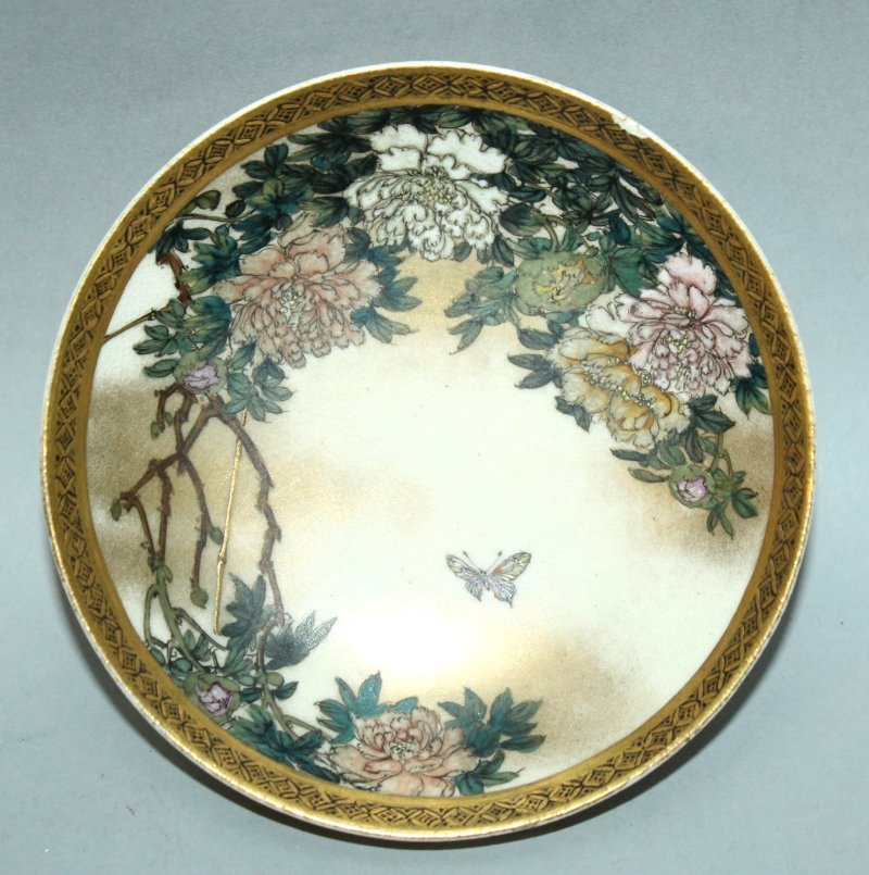 A SMALL JAPANESE MEIJI PERIOD KINKOZAN SATSUMA: A SMALL JAPANESE MEIJI PERIOD KINKOZAN SATSUMA EARTHENWARE FOOTED DISH, the interior painted with a butterfly hovering above peony, the underside rim with ho-ho phoenix and an original Kinkozan label,
