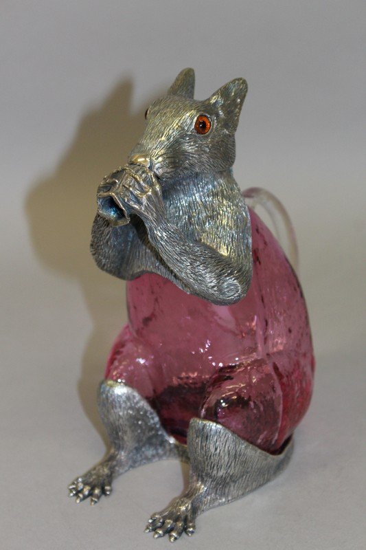 A GOOD NOVELTY PLATE MOUNTED SQUIRREL CLARET JUG,: A GOOD NOVELTY PLATE MOUNTED SQUIRREL CLARET JUG, eating a fruit, with ruby glass body. 7ins high. £300-400