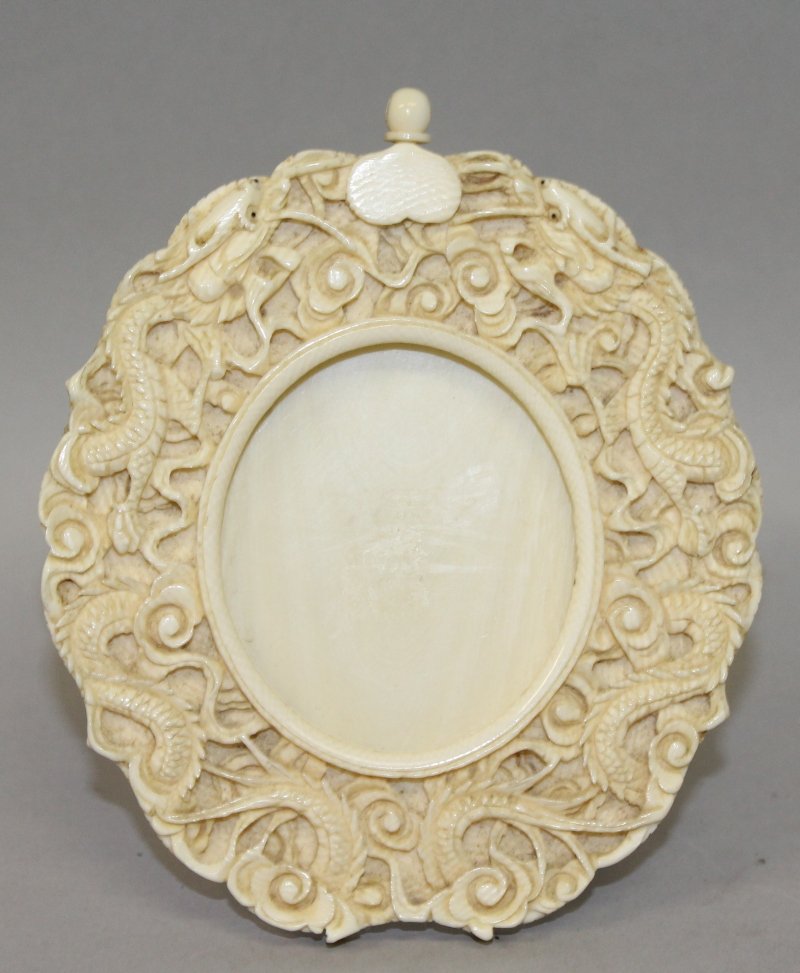 A 19TH/20TH CENTURY CHINESE IVORY OVAL PICTURE FRAME,: A 19TH/20TH CENTURY CHINESE IVORY OVAL PICTURE FRAME, circa 1900, the rim carved in deep relief with two sinuous dragons amidst cloud scrolls, 4.5in high x 3.9in wide. John Nicholsons Auctioneers do n