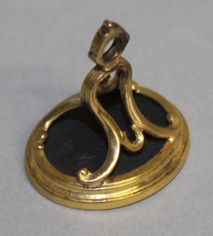 A GEORGIAN GILT METAL MOUNTED FOB SEAL, the oval basalt: A GEORGIAN GILT METAL MOUNTED FOB SEAL, the oval basalt intaglio incised with a male portrait profile, with bell shaped scroll surmount. 2.3cms long.