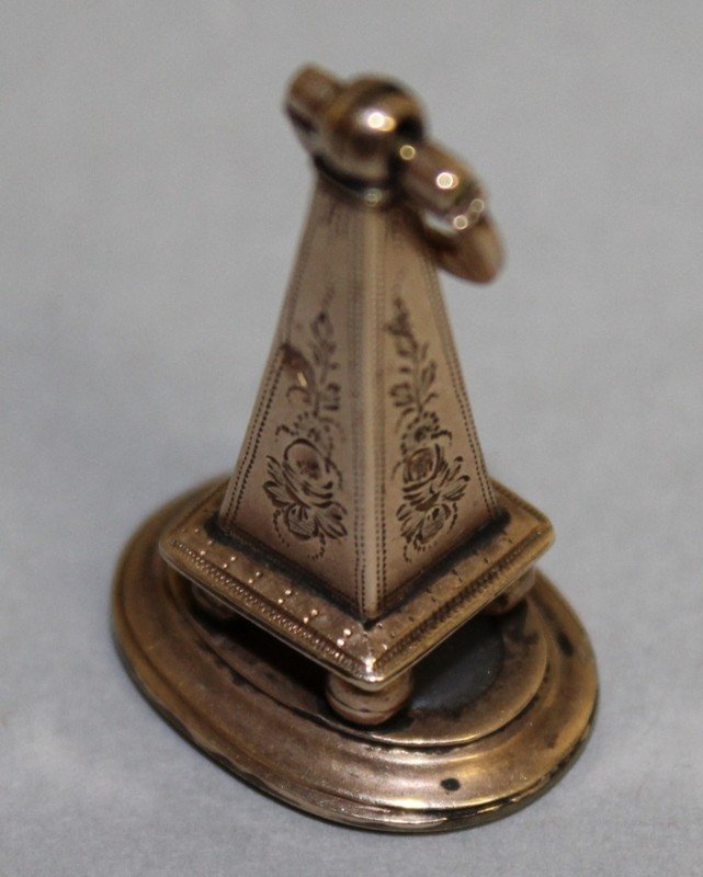 A GEORGIAN ROSE GOLD FOB SEAL, the oval chalcedony: A GEORGIAN ROSE GOLD FOB SEAL, the oval chalcedony intaglio inscribed €œVERITE€ beneath a hand holding a quill and a heart with foliate engraved obelisk surmount. 3.3cms long.