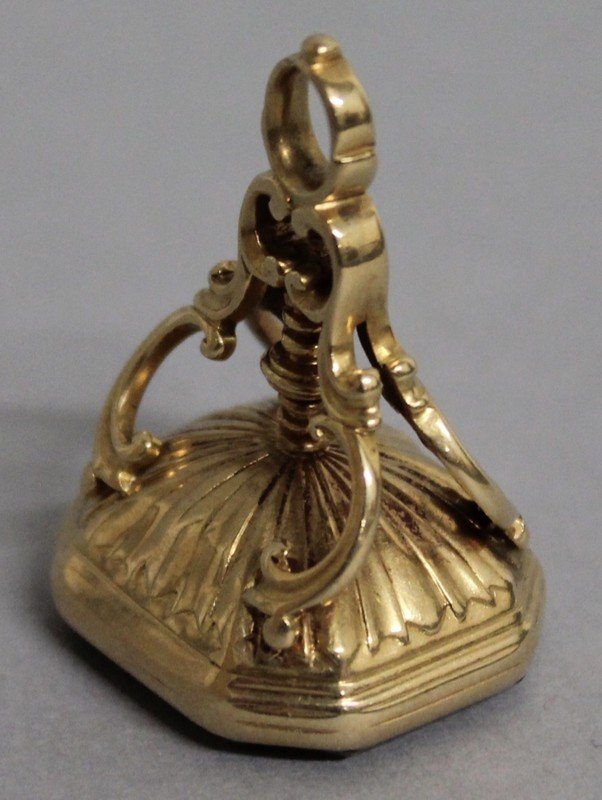 A GEORGIAN GOLD MOUNTED FOB SEAL, the canted: A GEORGIAN GOLD MOUNTED FOB SEAL, the canted rectangular cornelian intaglio with incised armorial, and fluted domed mount with scroll surmount. 3cms long.