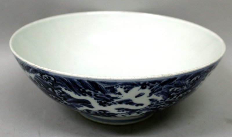 A CHINESE MING STYLE BLUE & WHITE PORCELAIN BOWL, the: A CHINESE MING STYLE BLUE & WHITE PORCELAIN BOWL, the rounded sides decorated with dragons reserved in white against a ground of overlapping foaming waves, the base with a six-character Xuande mark, 9