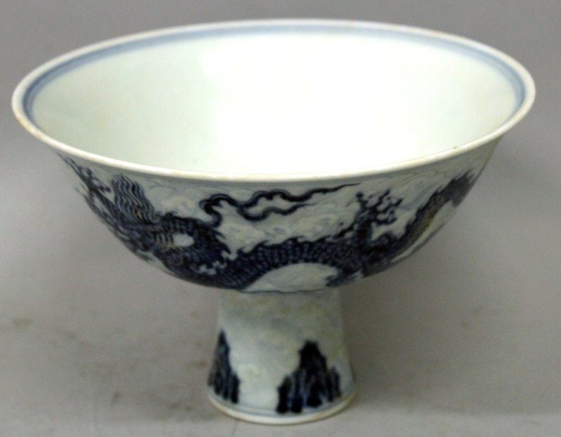 A CHINESE MING STYLE BLUE & WHITE PORCELAIN STEM BOWL,: A CHINESE MING STYLE BLUE & WHITE PORCELAIN STEM BOWL, the sides decorated with two dragons above stylised rockwork and reserved against pale overlapping waves, the interior with a six-character Xuand