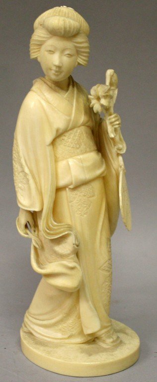 A GOOD JAPANESE MEIJI PERIOD IVORY OKIMONO OF A BIJIN,: A GOOD JAPANESE MEIJI PERIOD IVORY OKIMONO OF A BIJIN, standing in engraved robes, holding a bunch of flowers in one hand and a pair of scissors in the other, her fan hanging from her arm, 6.9in high.
