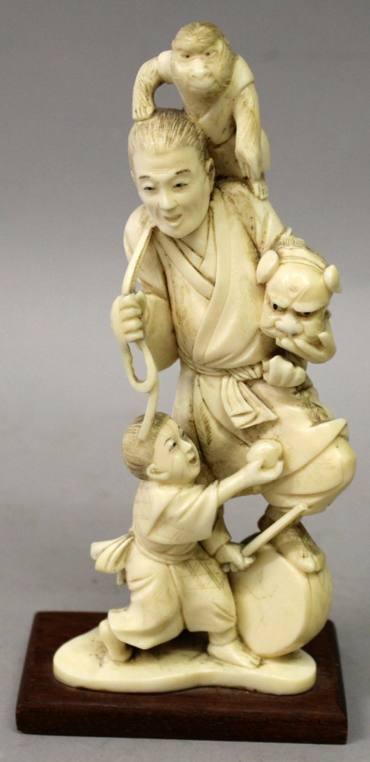 A JAPANESE MEIJI PERIOD IVORY OKIMONO OF A STREET: A JAPANESE MEIJI PERIOD IVORY OKIMONO OF A STREET PERFORMER, together with a fixed wood stand, the man in the company of a child and a monkey, his foot resting on a drum, a shi-shi costume held in his