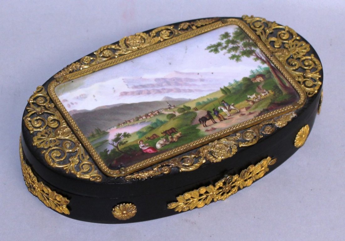 A 19TH CENTURY CONTINENTAL OVAL BOX AND COVER with: A 19TH CENTURY CONTINENTAL OVAL BOX AND COVER with inset porcelain top, mountainous scene with animals and figures, and gilt mounts. 6.5ins wide.