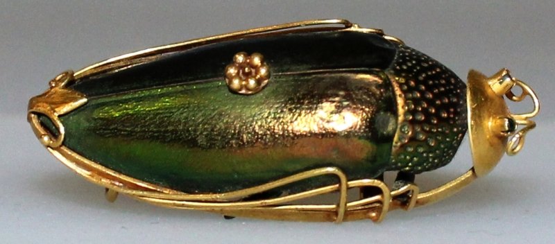 A CHINESE GOLD MOUNTED BEETLE SHELL BROOCH, weighing: A CHINESE GOLD MOUNTED BEETLE SHELL BROOCH, weighing 4.2gm.in total with shell , the beetle with iridescent appearance, the mount with impressed character mark, 1.6in long.