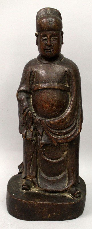 A 16TH CENTURY CHINESE MING DYNASTY CARVED WOOD FIGURE: A 16TH CENTURY CHINESE MING DYNASTY CARVED WOOD FIGURE OF AN OFFICIAL, standing in flowing robes on an oval plinth, 12.4in high.