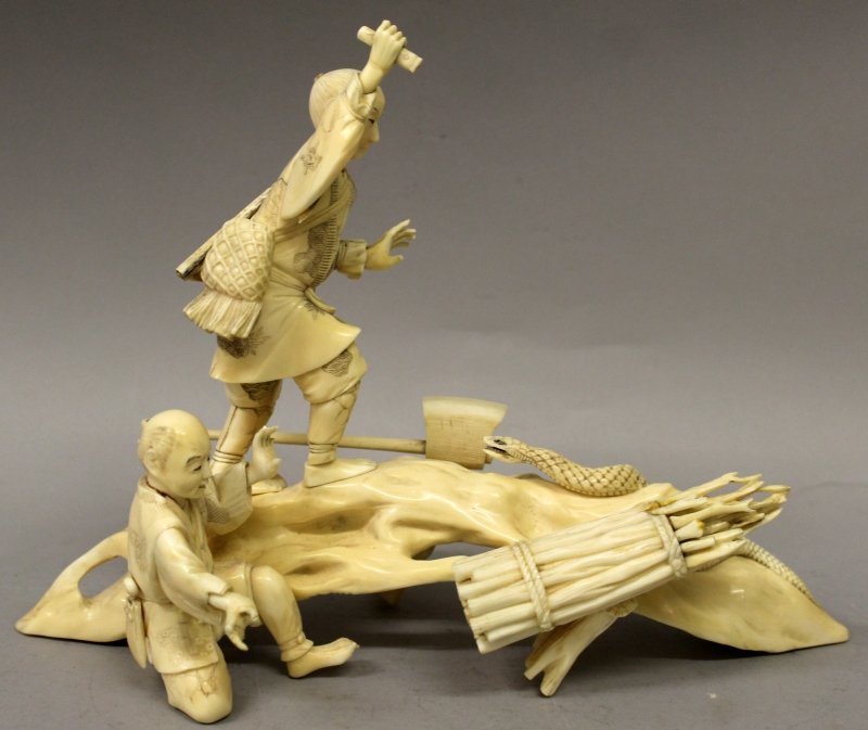 A JAPANESE MEIJI PERIOD SECTIONAL IVORY OKIMONO, in the: A JAPANESE MEIJI PERIOD SECTIONAL IVORY OKIMONO, in the form of two woodcutters on a curved trunk defending themselves from a large attacking snake, 11.25in long & 8.25in high. John Nicholsons Auction