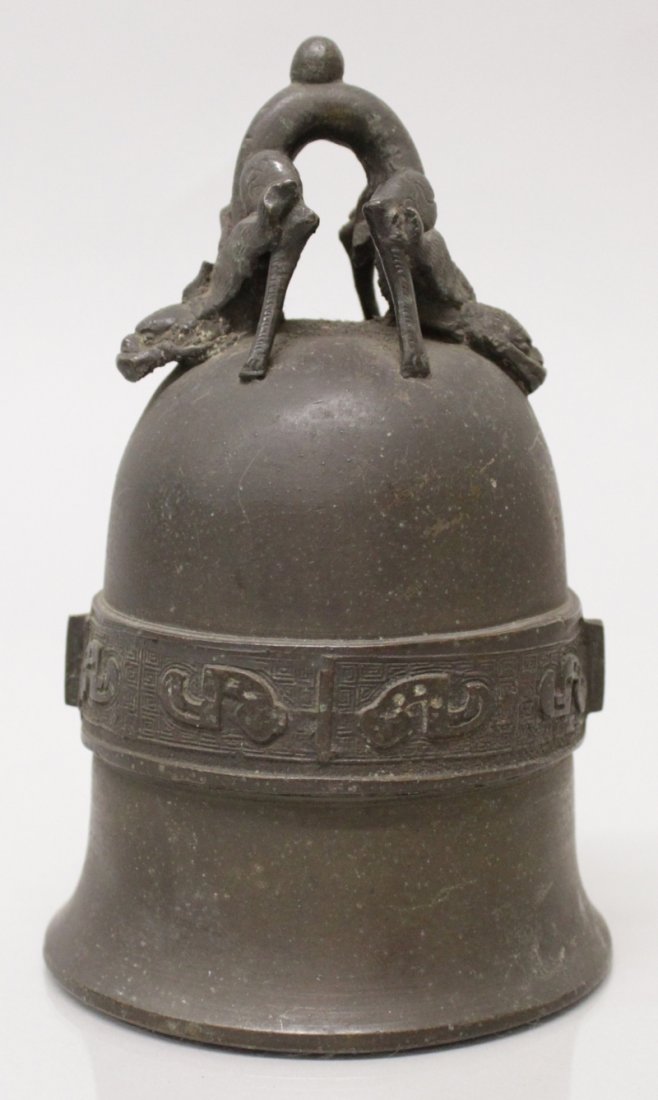 A WELL CAST CHINESE BRONZE BELL, 19th Century or: A WELL CAST CHINESE BRONZE BELL, 19th Century or earlier, the loop handle formed from double chilong, the side with a band of archaic design, 4.25in diameter at rim & 6.7in high overall.